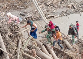 seorang prajurit TNI, Serma Ilham, Babinsa Kodim 0111/Bireuen, menggendong seorang ibu lanjut usia melintasi tumpukan puing, kayu besar, dan material banjir yang berserakan di Desa Awe Geutah, Kecamatan Peusangan Siblah Krueng, Kabupaten Bireuen, pada Selasa 2/12/2025