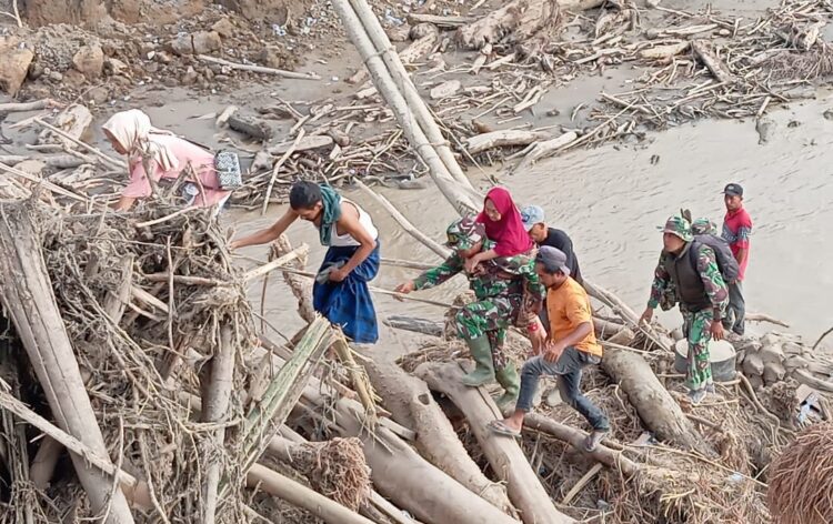 seorang prajurit TNI Serma Ilham Babinsa Kodim 0111Bireuen menggendong seorang ibu lanjut usia melintasi tumpukan puing kayu besar dan material banjir yang berserakan di Desa Awe Geutah Kecamatan Peusangan Siblah Krueng Kabupaten Bireuen pada Selasa 2122025