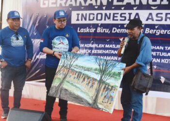 Pelukis Aceh, Salaudin, menyerahkan sebuah lukisan kepada Plt Ketua DPD Partai Demokrat Aceh, Rian Syaf, pada peringatan HUT ke-25 Partai Demokrat di kawasan Pantai Tibang, Banda Aceh, Jumat (31/7/2026). FOTO/Istimewa